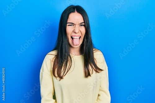 Young brunette woman wearing casual sweatshirt sticking tongue out happy with funny expression. emotion concept.