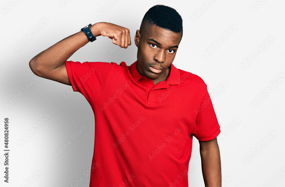 Young african american man wearing casual red t shirt strong person showing arm muscle, confident and proud of power Young african american man wearing casual red t shirt strong person showing arm muscle, confident and proud of power