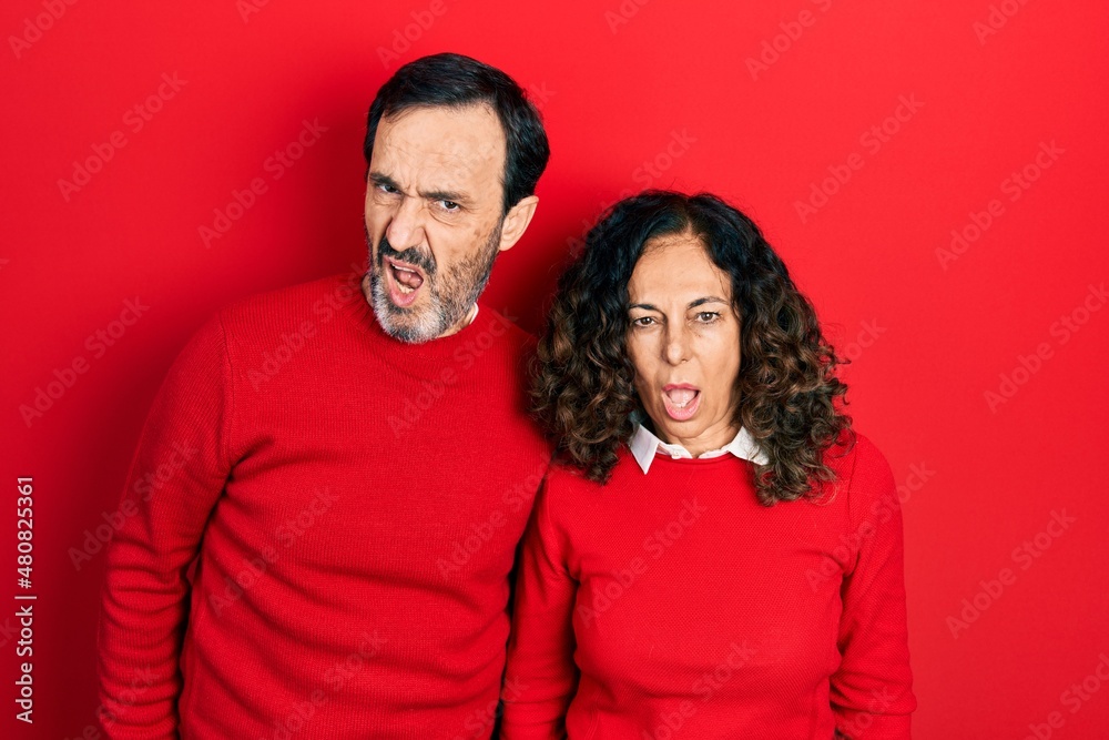Middle age couple of hispanic woman and man hugging and standing together in shock face, looking skeptical and sarcastic, surprised with open mouth Middle age couple of hispanic woman and man hugging and standing together in shock face, looking skeptical and sarcastic, surprised with open mouth