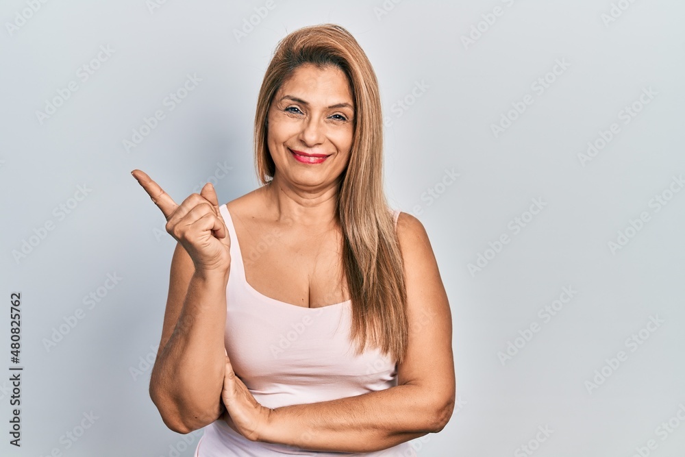 Middle age hispanic woman wearing casual style with sleeveless shirt with a big smile on face, pointing with hand and finger to the side looking at the camera. Middle age hispanic woman wearing casual style with sleeveless shirt with a big smile on face, pointing with hand and finger to the side looking at the camera.