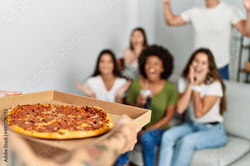Group of young friends smiling happy waiting for italian pizza at home.
