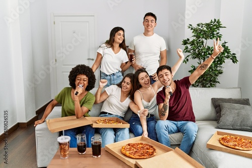 Group of young friends having party eating italian pizza and singing song at home.
