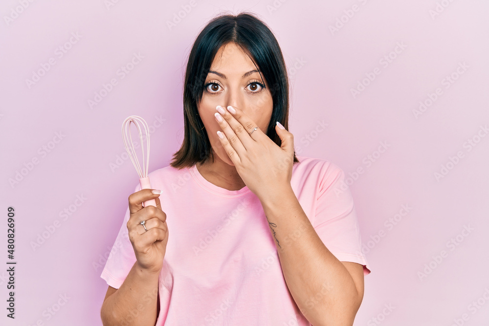 Young hispanic woman cooking using baker whisk covering mouth with hand, shocked and afraid for mistake. surprised expression Young hispanic woman cooking using baker whisk covering mouth with hand, shocked and afraid for mistake. surprised expression