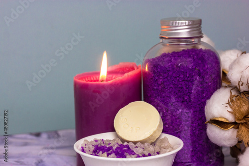 Violet lavender sea salt for bath in the bottle, a burning candle and branch of cotton flower. A bar of soap or dry shampoo. Face and body care, spa treatments concept. Cosmetic products. Copy space.