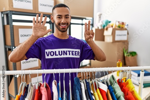 African american man wearing volunteer t shirt at donations stand showing and pointing up with fingers number seven while smiling confident and happy.