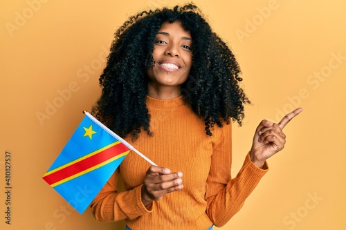African american woman with afro hair holding democratic republic of the congo flag smiling happy pointing with hand and finger to the side photo