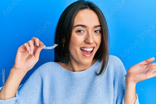 Young hispanic girl holding invisible aligner orthodontic celebrating achievement with happy smile and winner expression with raised hand photo