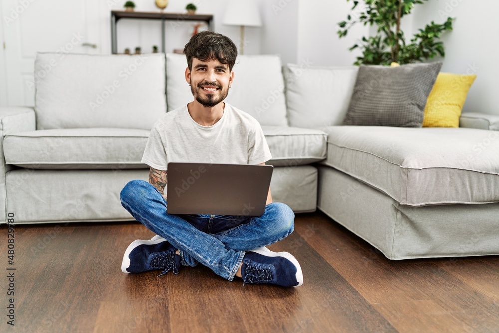 Young hispanic man using laptop sitting on the floor at home.