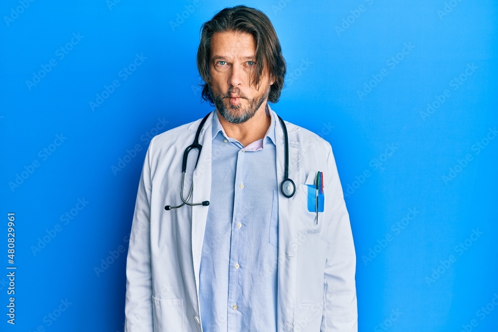 Middle age handsome man wearing doctor uniform and stethoscope making fish face with lips, crazy and comical gesture. funny expression. Middle age handsome man wearing doctor uniform and stethoscope making fish face with lips, crazy and comical gesture. funny expression.