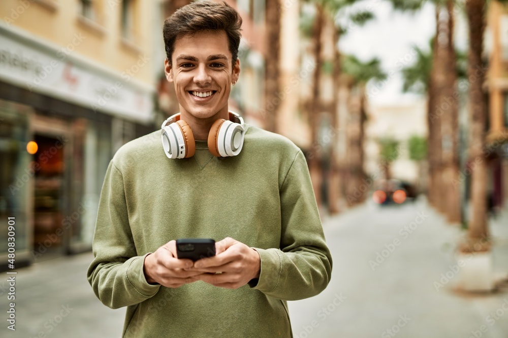 Young hispanic man smiling happy using smartphone and headphones at the city. Young hispanic man smiling happy using smartphone and headphones at the city.