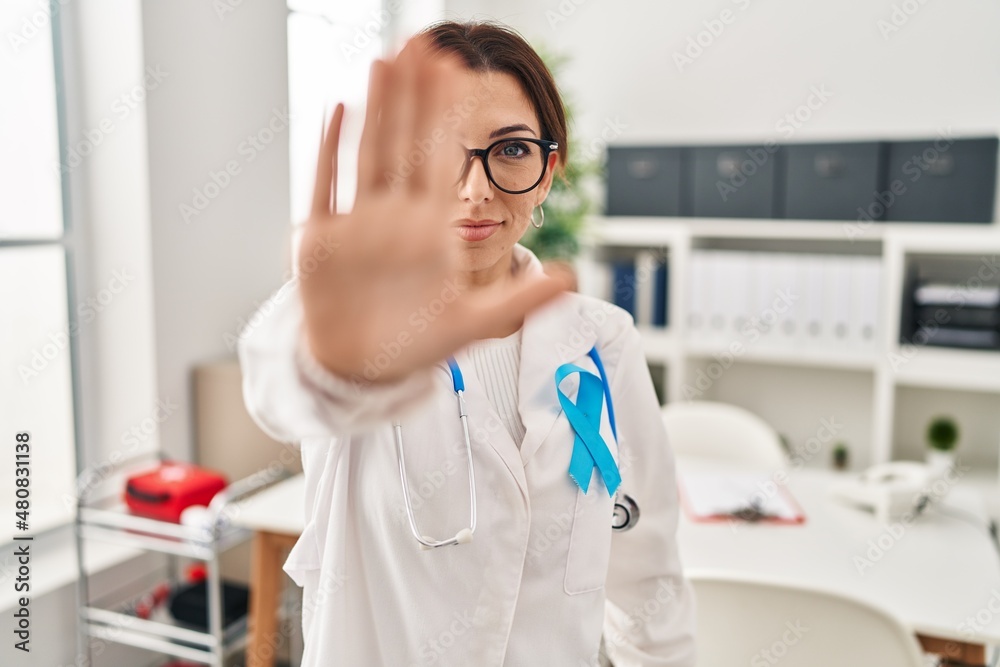 Young brunette doctor woman wearing stethoscope at the clinic doing stop sing with palm of the hand. warning expression with negative and serious gesture on the face.