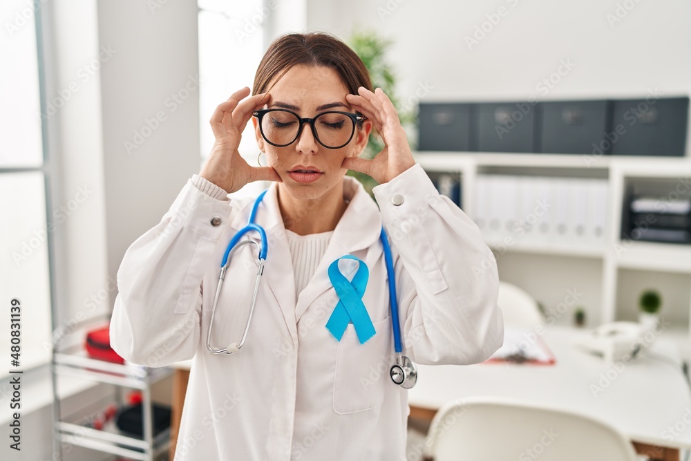 Young brunette doctor woman wearing stethoscope at the clinic with hand on head for pain in head because stress. suffering migraine. Young brunette doctor woman wearing stethoscope at the clinic with hand on head for pain in head because stress. suffering migraine.