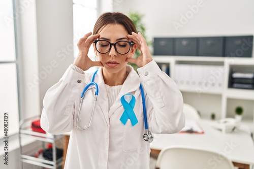 Young brunette doctor woman wearing stethoscope at the clinic with hand on head for pain in head because stress. suffering migraine.