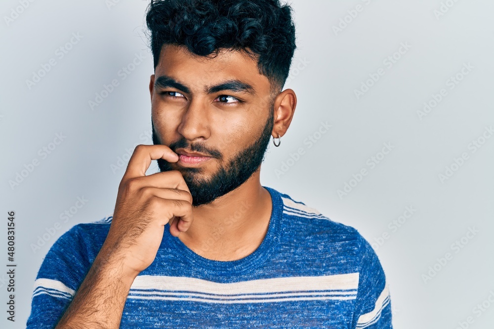 Arab man with beard wearing casual striped t shirt serious face thinking about question with hand on chin, thoughtful about confusing idea Arab man with beard wearing casual striped t shirt serious face thinking about question with hand on chin, thoughtful about confusing idea