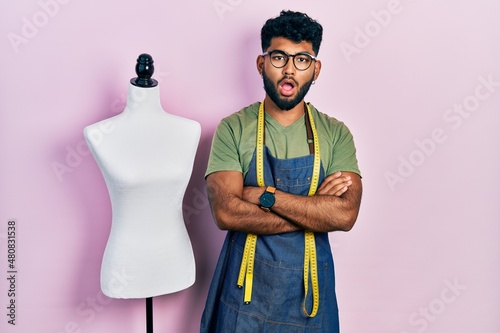 Arab man with beard dressmaker designer wearing atelier apron afraid and shocked with surprise and amazed expression, fear and excited face.