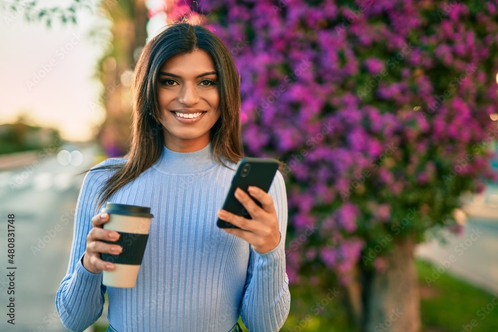 Young hispanic woman using smartphone and drinking a cup of coffee by the park Young hispanic woman using smartphone and drinking a cup of coffee by the park