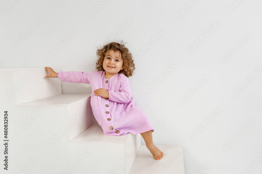 a little curly-haired girl in a purple dress plays on white steps a little curly-haired girl in a purple dress plays on white steps