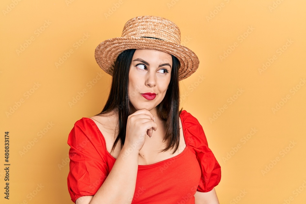 Young hispanic woman wearing summer hat with hand on chin thinking about question, pensive expression. smiling with thoughtful face. doubt concept. Young hispanic woman wearing summer hat with hand on chin thinking about question, pensive expression. smiling with thoughtful face. doubt concept.