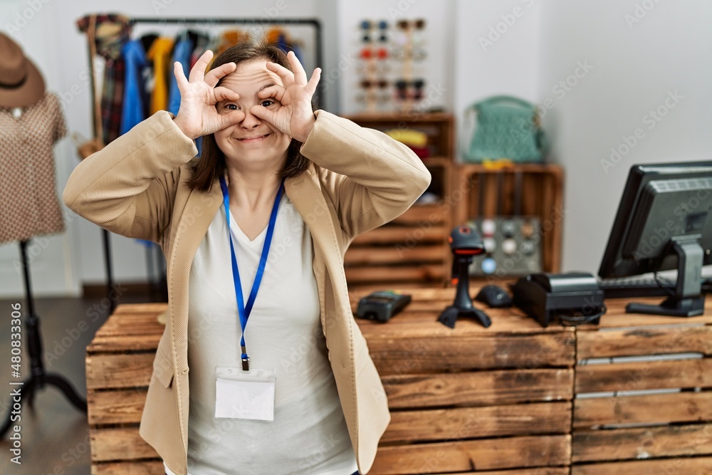 Young down syndrome woman working as manager at retail boutique doing ok gesture like binoculars sticking tongue out, eyes looking through fingers. crazy expression. Young down syndrome woman working as manager at retail boutique doing ok gesture like binoculars sticking tongue out, eyes looking through fingers. crazy expression.