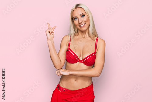 Young blonde woman wearing bikini smiling happy pointing with hand and finger to the side