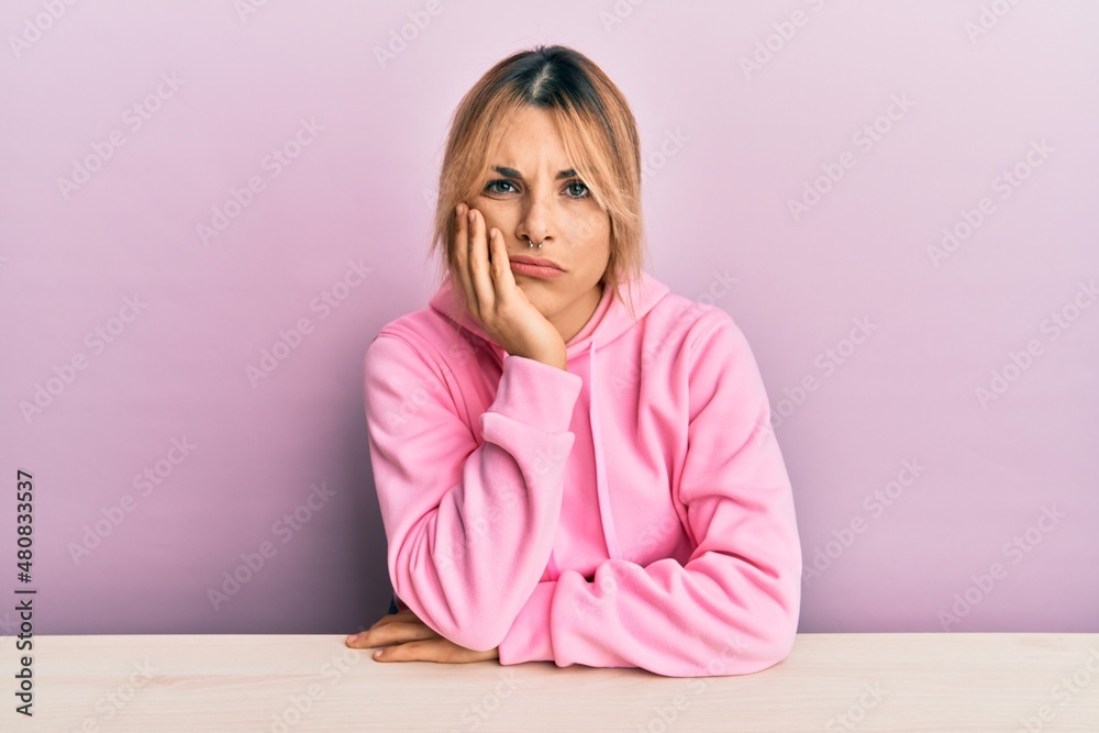 Young caucasian woman wearing casual clothes sitting on the table thinking looking tired and bored with depression problems with crossed arms. Young caucasian woman wearing casual clothes sitting on the table thinking looking tired and bored with depression problems with crossed arms.