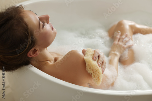 Beautiful woman with loofah taking bath indoors photo