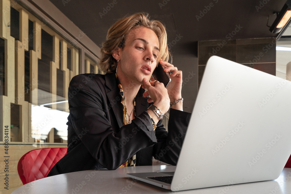 Elegant young businessman working with the computer during the day in the terrace of a cafe with a view of the city from above while drinking coffee