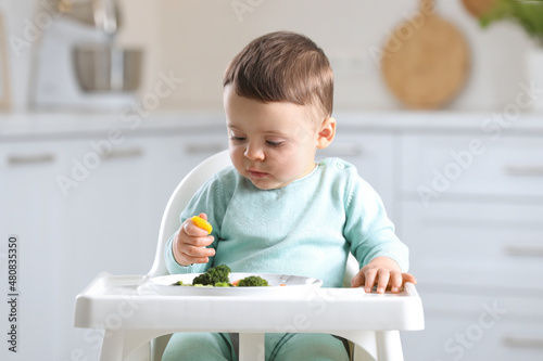 Cute little baby eating healthy food in high chair at home