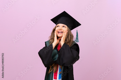 A joyful beautiful graduate looks up. a schoolgirl in a graduate's robe and a master's hat. the child is happy to receive an education in another country.