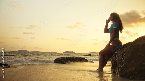 Woman leaning on a rock reef enjoying the warm golden sunset. Wo