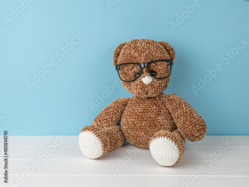 A beautiful knitted bear with glasses on a blue background. © kvladimirv