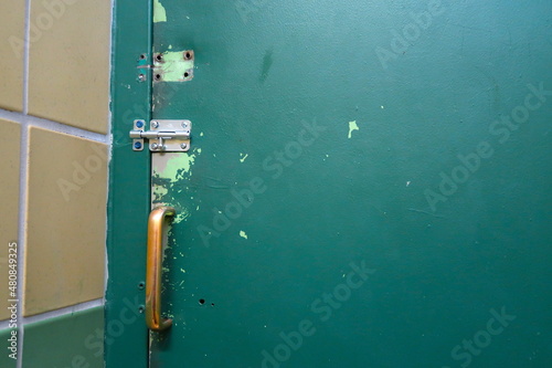 Old and worn green painted metal door with sliding bolt closure and brassy metal handle.  © Red Herring