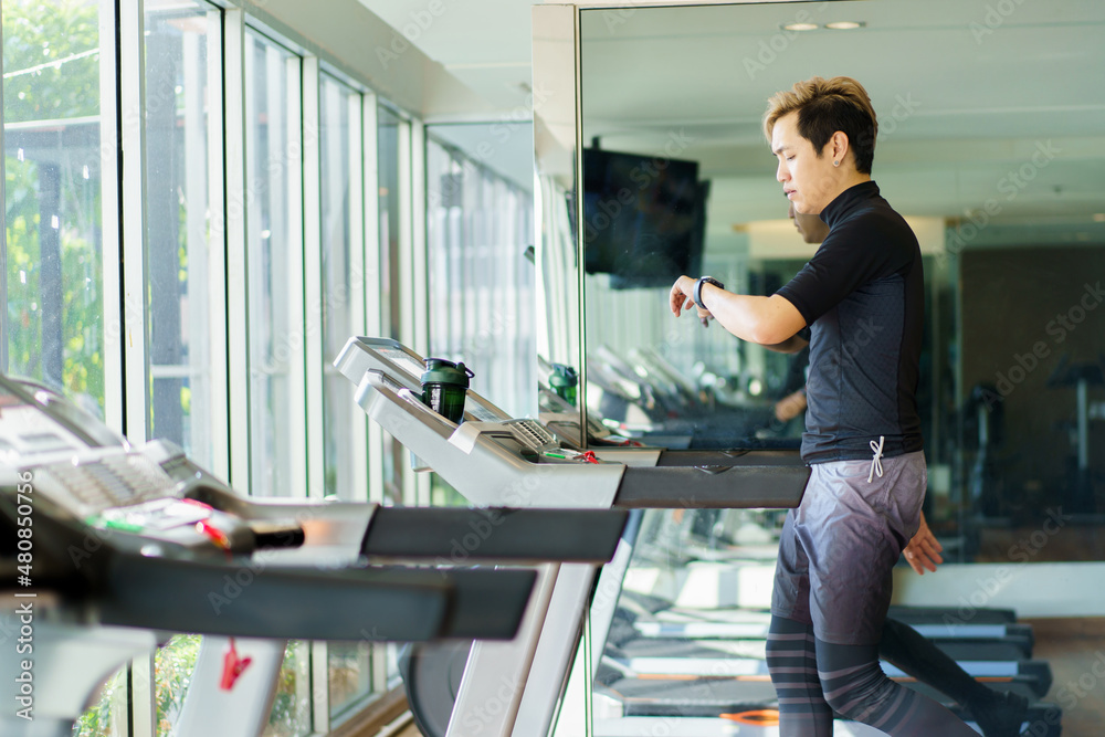 Active Asian sportsman making a cardio exercise by running on the treadmill machine in a fitness gym. Active Asian sportsman making a cardio exercise by running on the treadmill machine in a fitness gym.