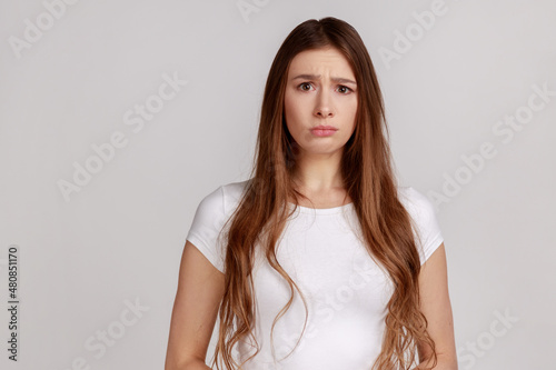 Photography Portrait of disappointed woman being upset of bad news, looking at camera with frowning face, expressing sadness, wearing white T-shirt