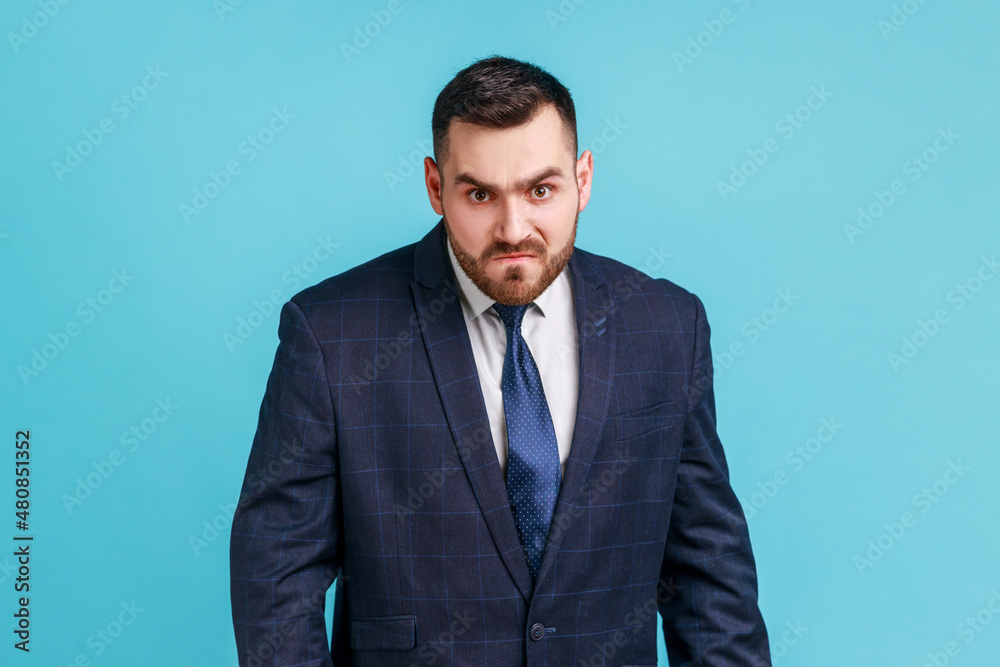 Angry handsome businessman wearing official style suit looking at camera, having aggressive facial expression, expressing negative, hatred. Indoor studio shot isolated on blue background. Angry handsome businessman wearing official style suit looking at camera, having aggressive facial expression, expressing negative, hatred. Indoor studio shot isolated on blue background.