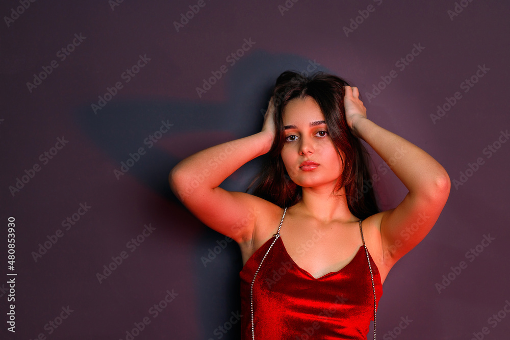 Fashion model young woman in colorful bright lights posing in sexual red clothes holding her hands on the head. Fashion model young woman in colorful bright lights posing in sexual red clothes holding her hands on the head.