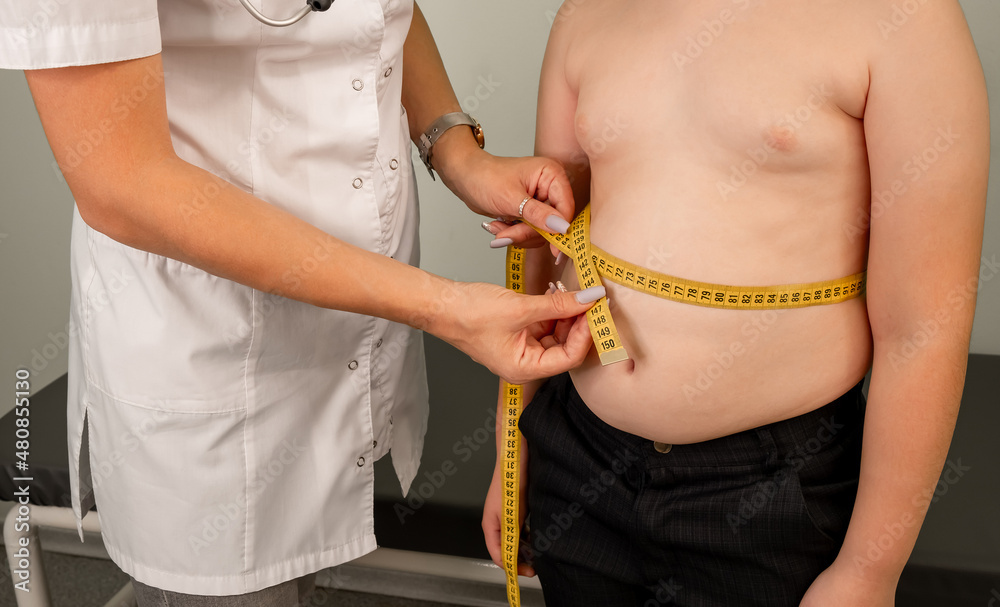 Concept of excessive weight, obese, dieting, overweight. Childhood obesity problem and weight loss. Doctor examining fat boy in clinic. Fat boy at a nutritionist appointment. Flabby skin on fat belly.