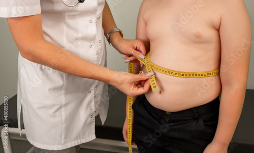 Obraz na płótnie Concept of excessive weight, obese, dieting, overweight. Childhood obesity problem and weight loss. Doctor examining fat boy in clinic. Fat boy at a nutritionist appointment. Flabby skin on fat belly. w salonie