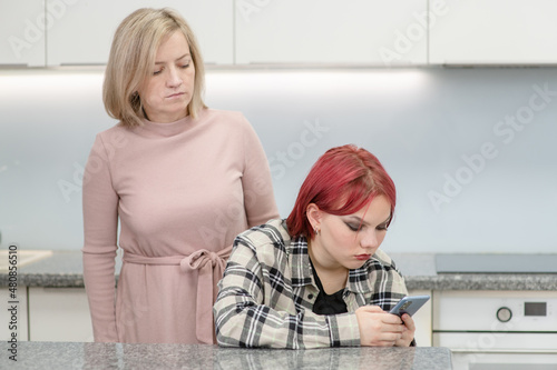 Fotografie Curious mother spying on what's on her daughter's phone screen