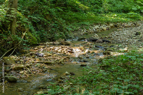 summer morning, walking along the bed of a mountain river that has become shallow by the end of summer and the upcoming autumn period and exposing its rocky bottom with clear water.
