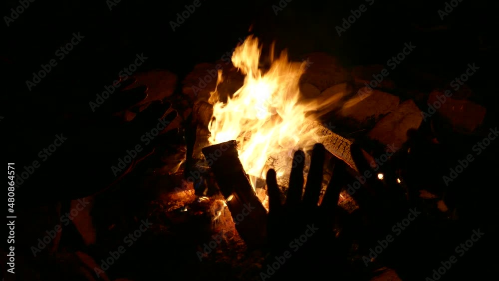 Campfire scene with silhouetted human hands warming by fire Campfire scene with silhouetted human hands warming by fire