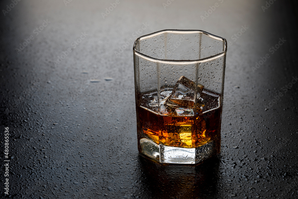 A glass of whiskey with ice cubes on the table close-up. A glass of whiskey with ice cubes on the table close-up.