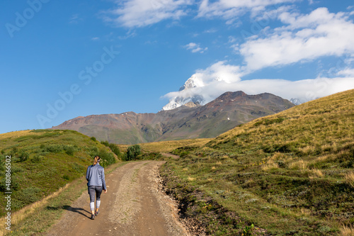 A woman walking on a panoramic hiking trail leading to the Koruldi Lakes in the Greater Caucasus Mountain Range in Georgia, Upper Svanet Region. Panoramic view on the Ushba mountain peaks. Wanderlust.