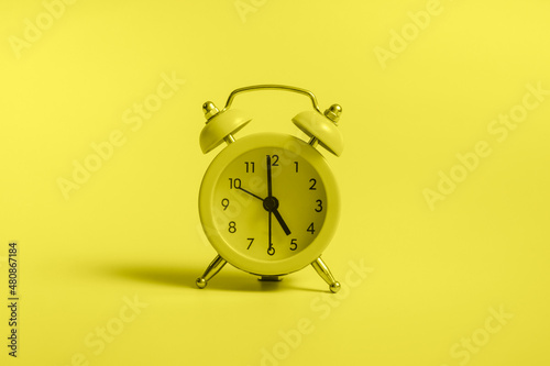 Yellow alarm clock with graduation cap on blue background closeup with copy space