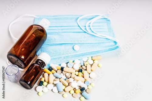 Brown bottles, a lot of colorful medicines and pills, a medical mask. Brown glass medical bottles for potions and various medicines. Composition on a light background.