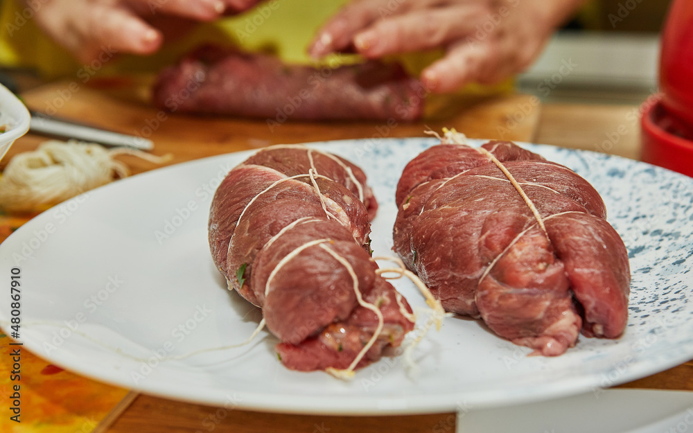 Meat rolls tied with string are on plate ready to be fried. French gourmet cuisine