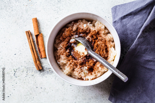 Scandinavian rice porridge with cinnamon and butter in white bowl on gray background. Norwegian cuisine concept.