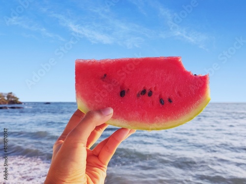 Holding a slice of bitten watermelon with blue sky and sea background