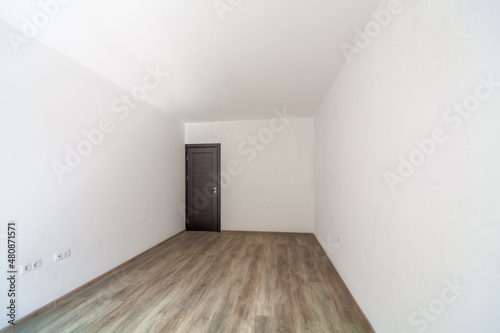 Closed wooden door in empty bright room. New home interior. Wooden floor. White walls