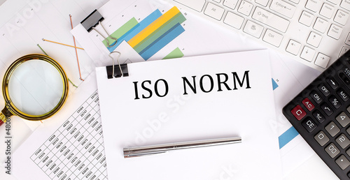 ISO NORM text on the white paper on the light background with charts paper ,keyboard and calculator